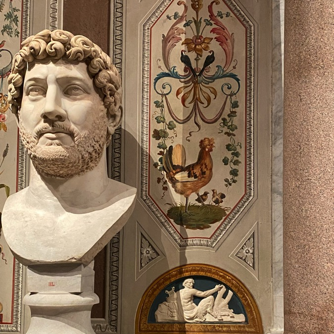 A hen among grotesqueries with a marble portrait bust of a bearded man on the left