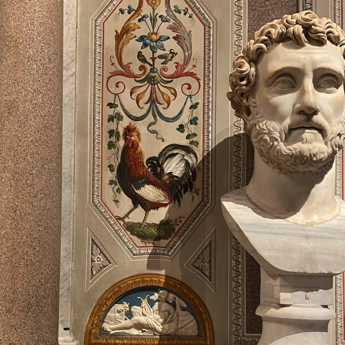 A rooster among grotesqueries with a marble portrait bust of a bearded man on the right