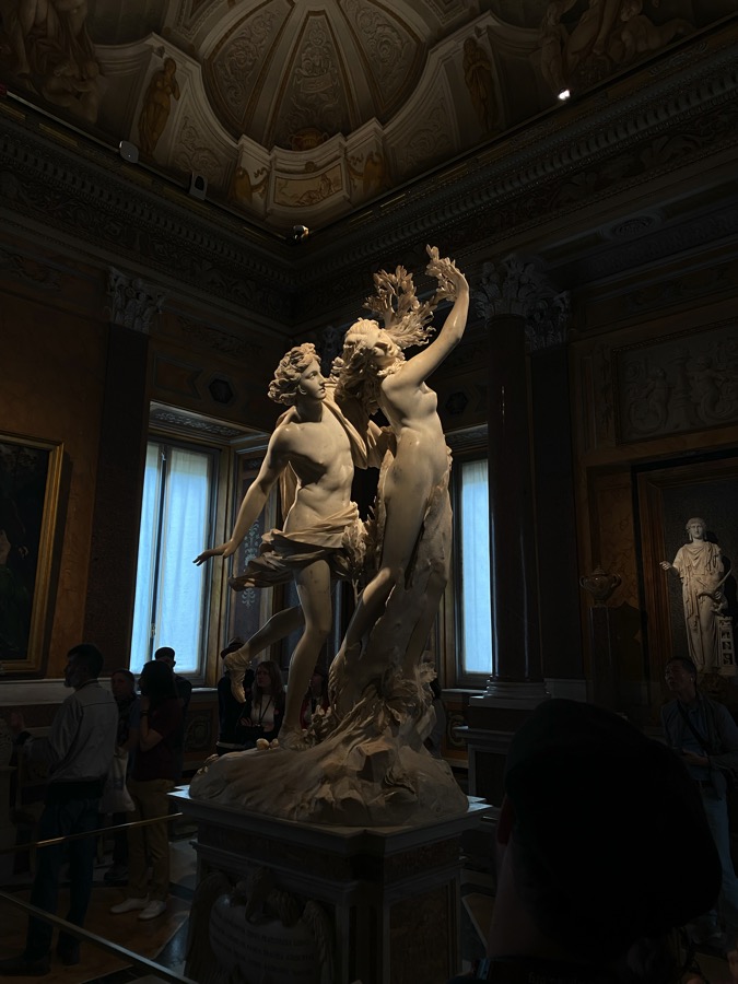 A white marble statue of Apollo and Daphne by Gian Lorenzo Bernini. Daphne is in the process of becoming a tree, her fingers are leaves, her toes roots, and her skin is turning to bark