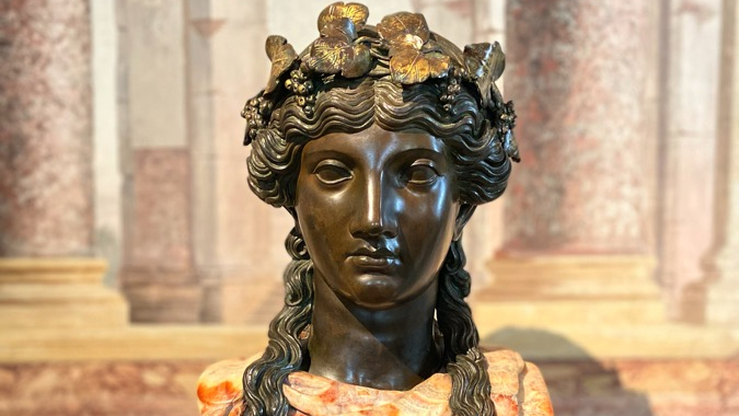 A bronze portrait bust of a woman with wavy hair garlanded with vine leaves