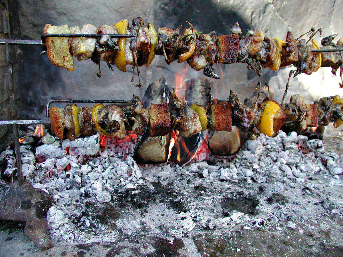 Small birds roasting on a spit in front of glowing embers