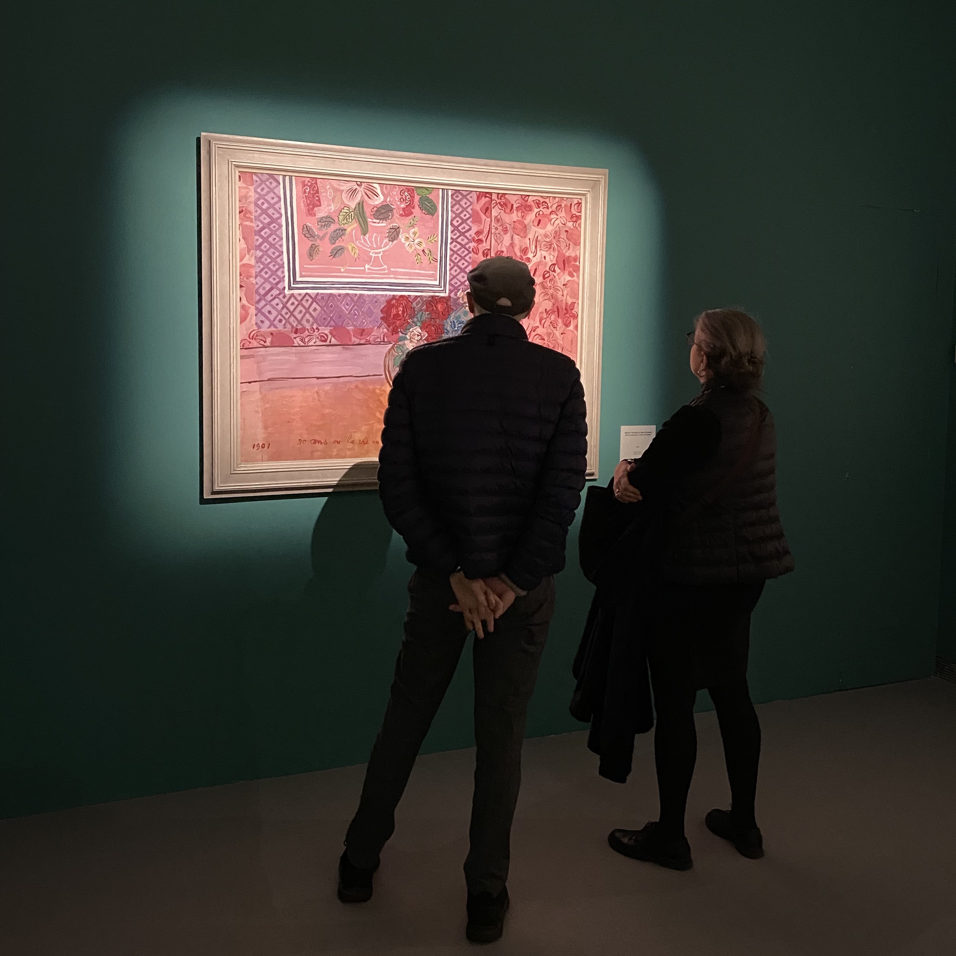 Two people in front of a pink still life, hung on a dark green wall