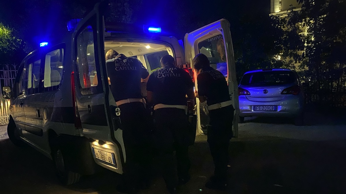 A white police van with blue lights on the roof and three police officers filling in forms on the back shelf