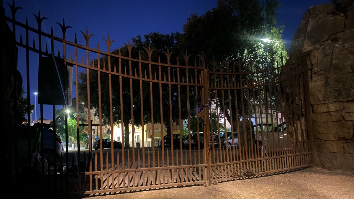 A large iron gate, locked shut, at night