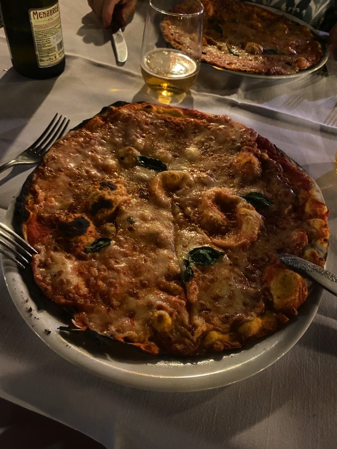 A pizza margherita and a half-full glass of beer