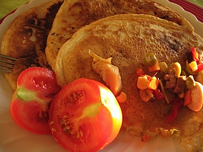 A plate of sourdough pancakes with a ripe, halved tomato and some other bits of pickles