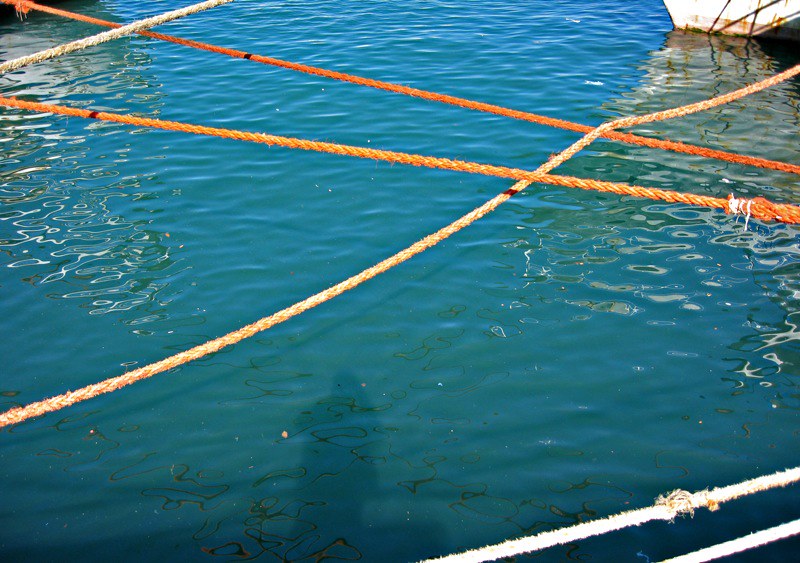 A harbour with fishing boats and ropes stretched between them casting shadows on the water