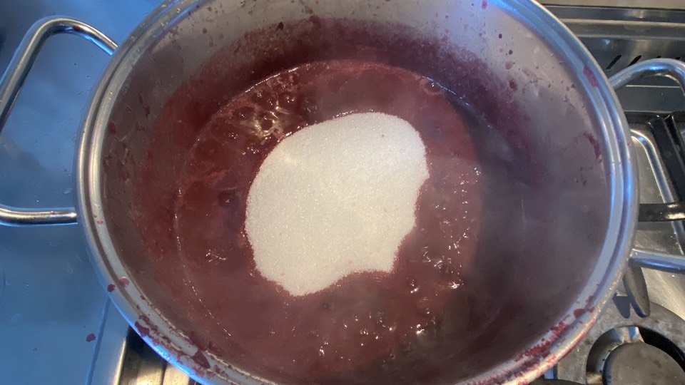 White sugar tipped into the purple juice and skins