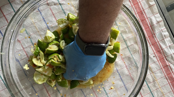 A hand wearing a blue nitrile glove squishing wedges of lime with salt