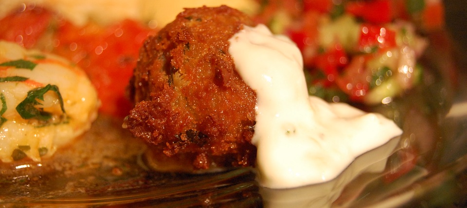 A single falafel on a plate with a scoop of, presumably, tahini sauce