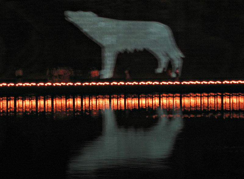 Blurred image of a howling wolf projected onto the embankment of the Tiber, with candles