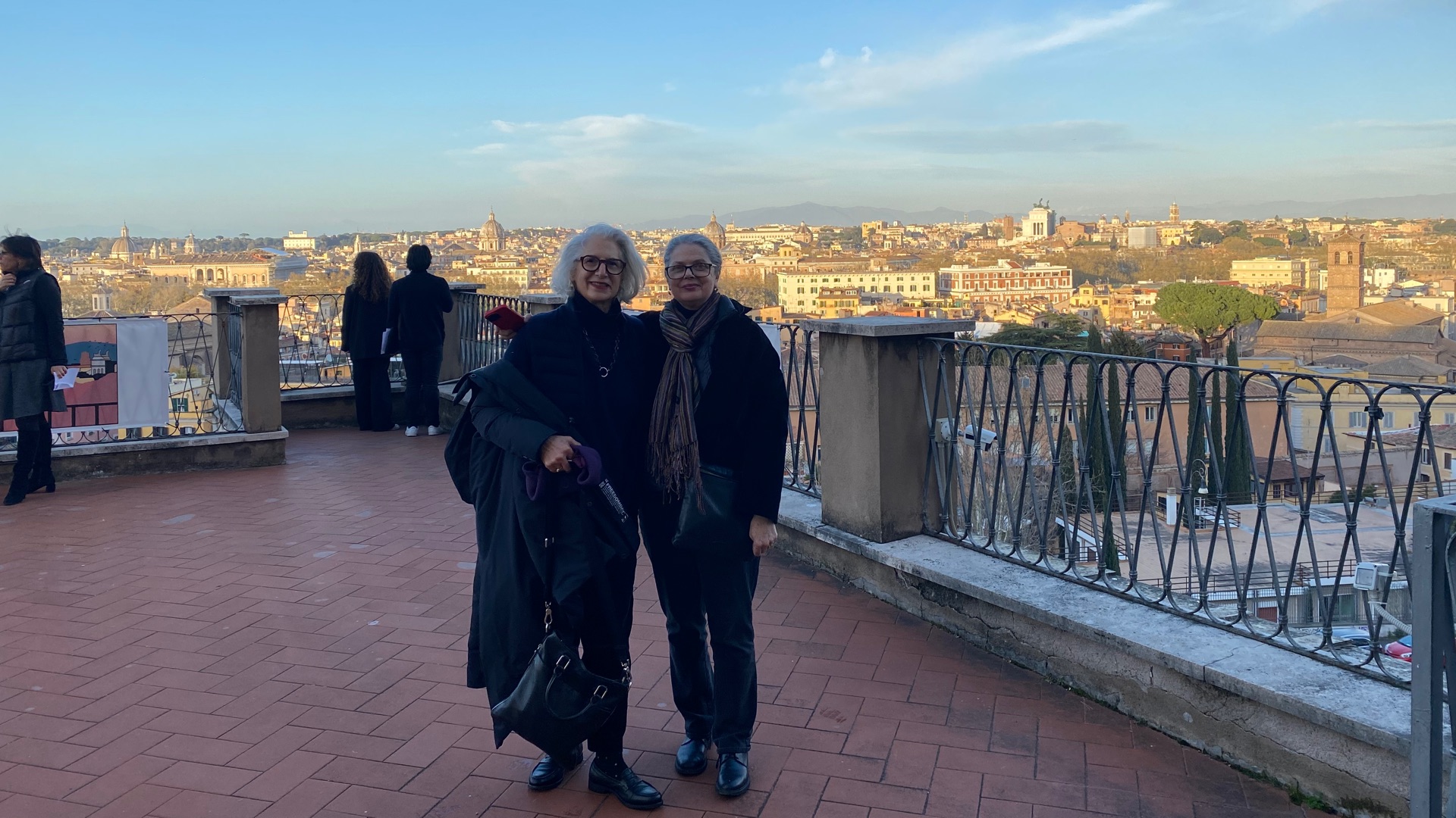 Two women standing with their backs to a view of Rome in the evening light