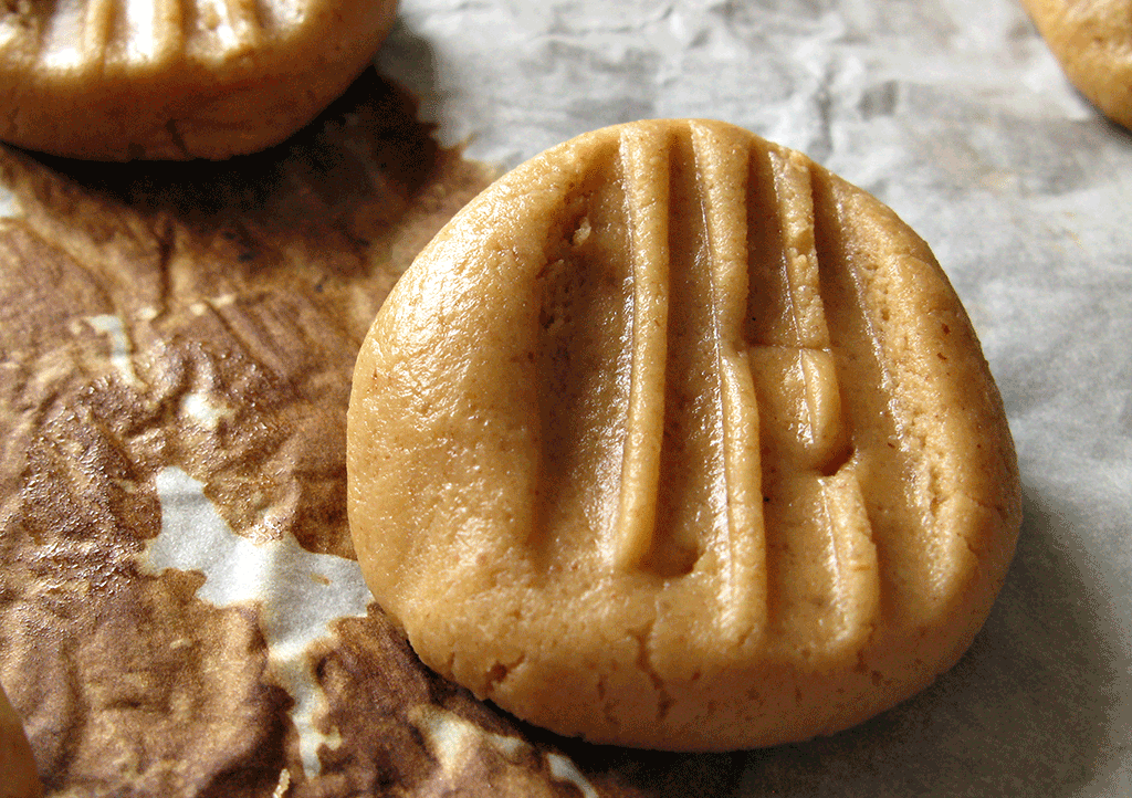 One peanut-butter cookie before baking with marks of the fork used to squish the ball of cookie dough