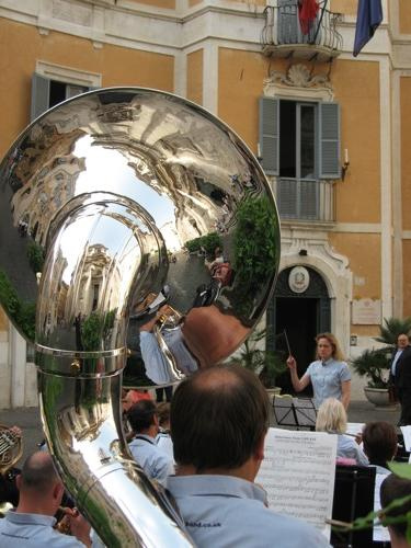 Reflections in the bell of a polished Sousaphone with a woman conducting the band in the background