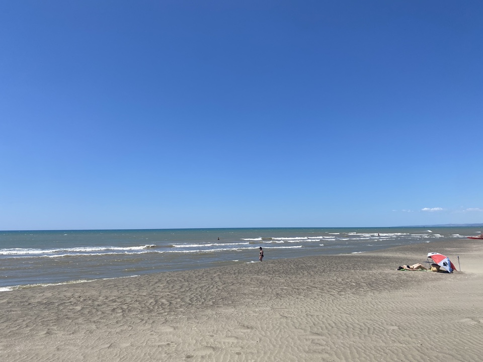 Wide view of an almost empty beach with very blue sky and murky inshore water