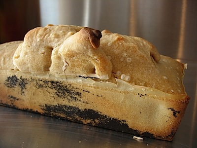 The finsihed loaf, with a large bubble arising from the top and black coating that may be Teflon soming unstick from the loaf tin