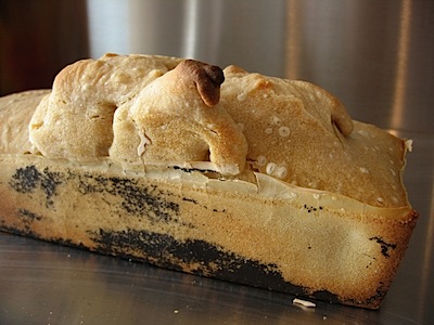 The finsihed loaf, with a large bubble arising from the top and black coating that may be Teflon soming unstick from the loaf tin