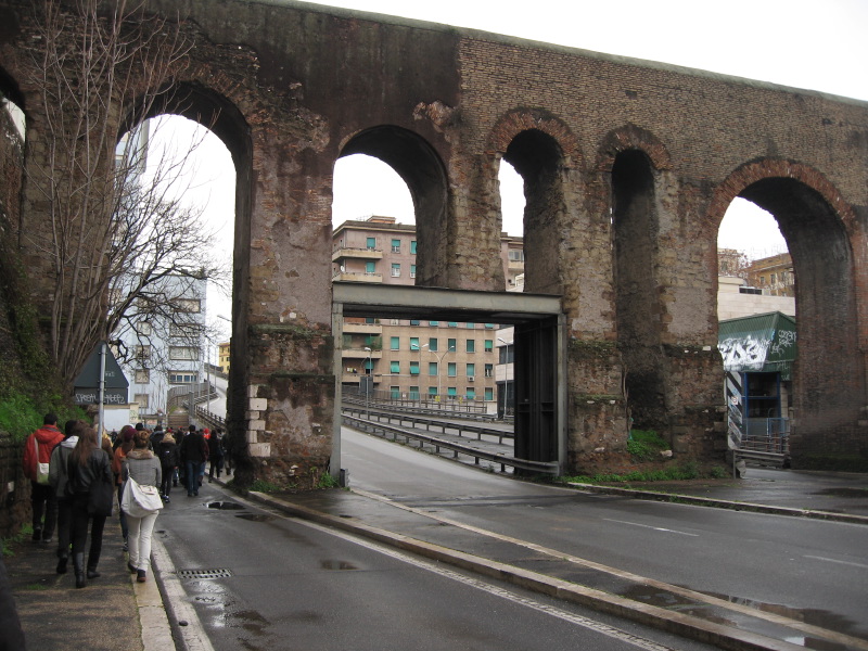 A Roman aquaduct with the pillar of one arch cut through to allow a large road to go under it.